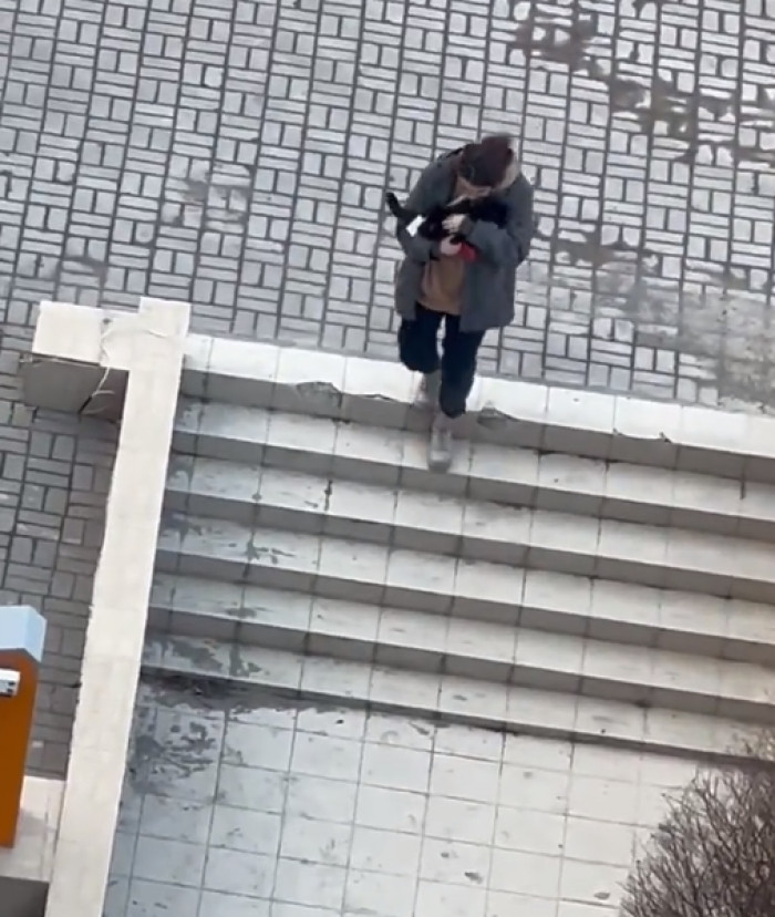 The video shows a young woman cradling a cat in her arms on the street.