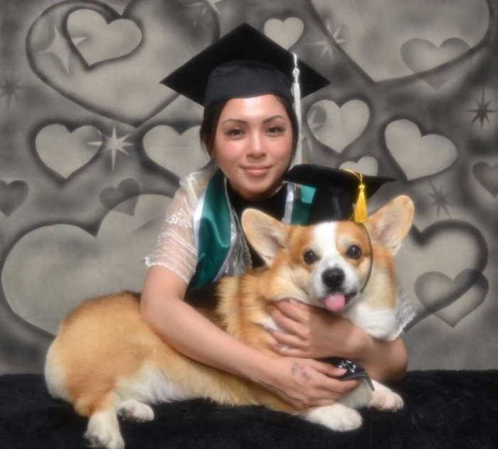 Student and dog sit together outdoors, smiling in graduation attire