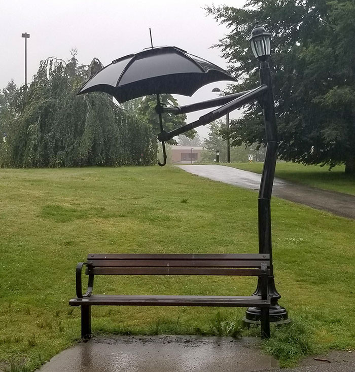 23. A lamp post holding up an umbrella for a bench spot