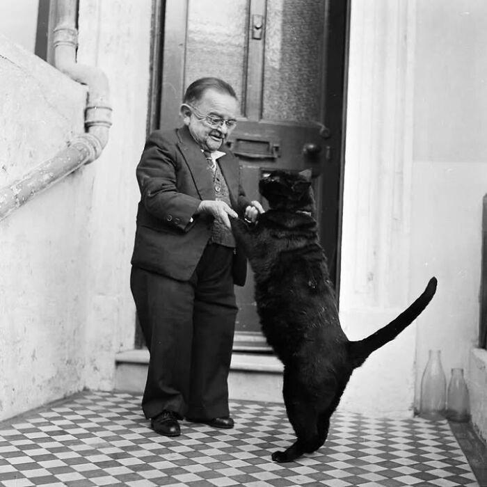 "Henry Behrens, once recognized as the world's smallest man at just 30 inches (76 cm) tall and weighing 32 pounds (14.5 kg), dances with his cat in the doorway of his home in Worthing, England, 1956."